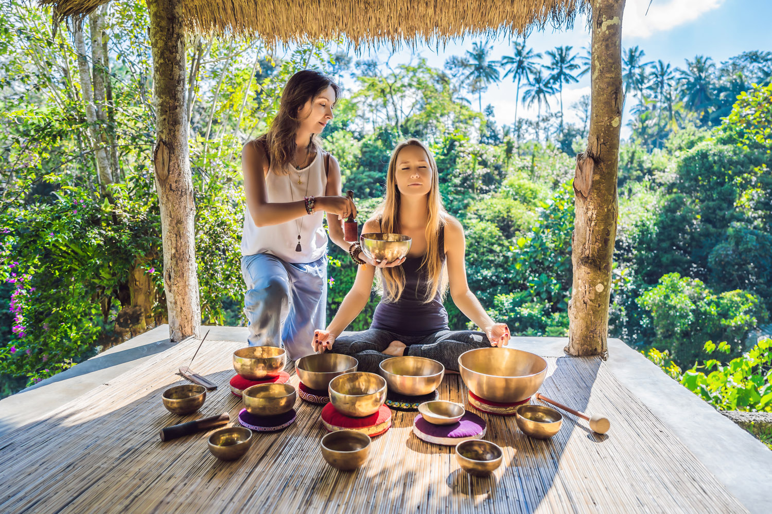 Nepal Buddha copper singing bowl at spa salon. Young beautiful woman doing massage therapy singing bowls in the Spa against a waterfall. Sound therapy, recreation, meditation, healthy lifestyle and body care concept.